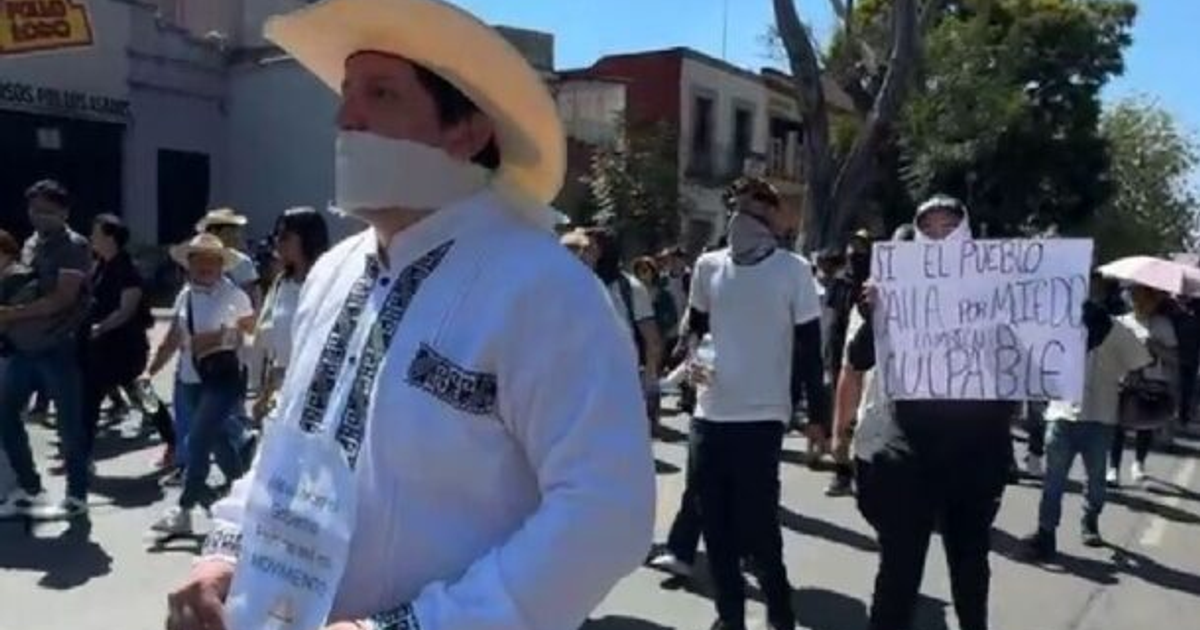 Hombre con camisa blanca y sombrero en marcha estudiantil en Morelia, sosteniendo un cartel de protesta.