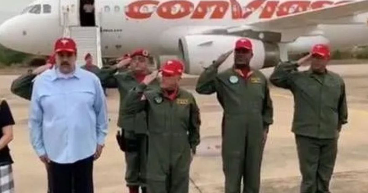 Grupo de personas en aeropuerto posando con avión al fondo, algunas en saludo militar, en un contexto de aviación militar.