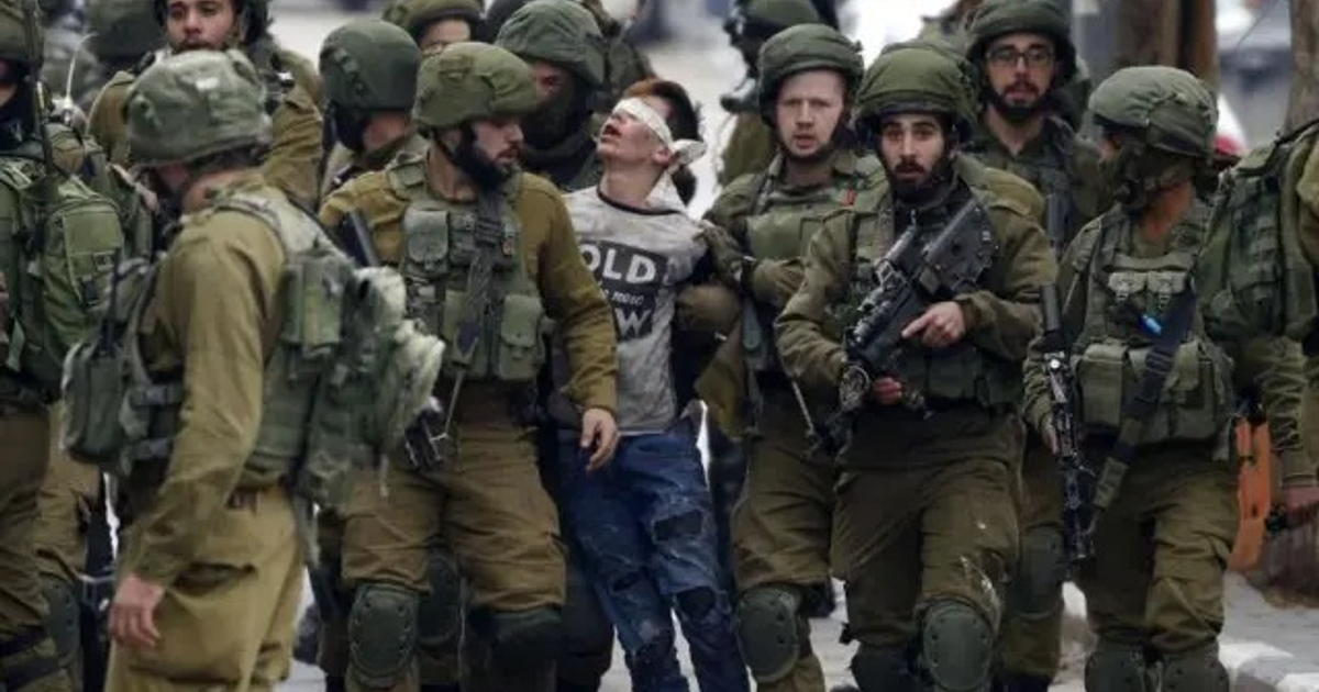 Soldados rodean a un prisionero con los ojos vendados en un entorno urbano, reflejando el conflicto en Cisjordania.