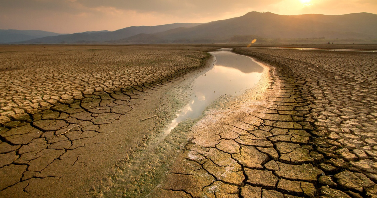Paisaje árido con terreno agrietado, corriente de agua y montañas al atardecer en Sinaloa.