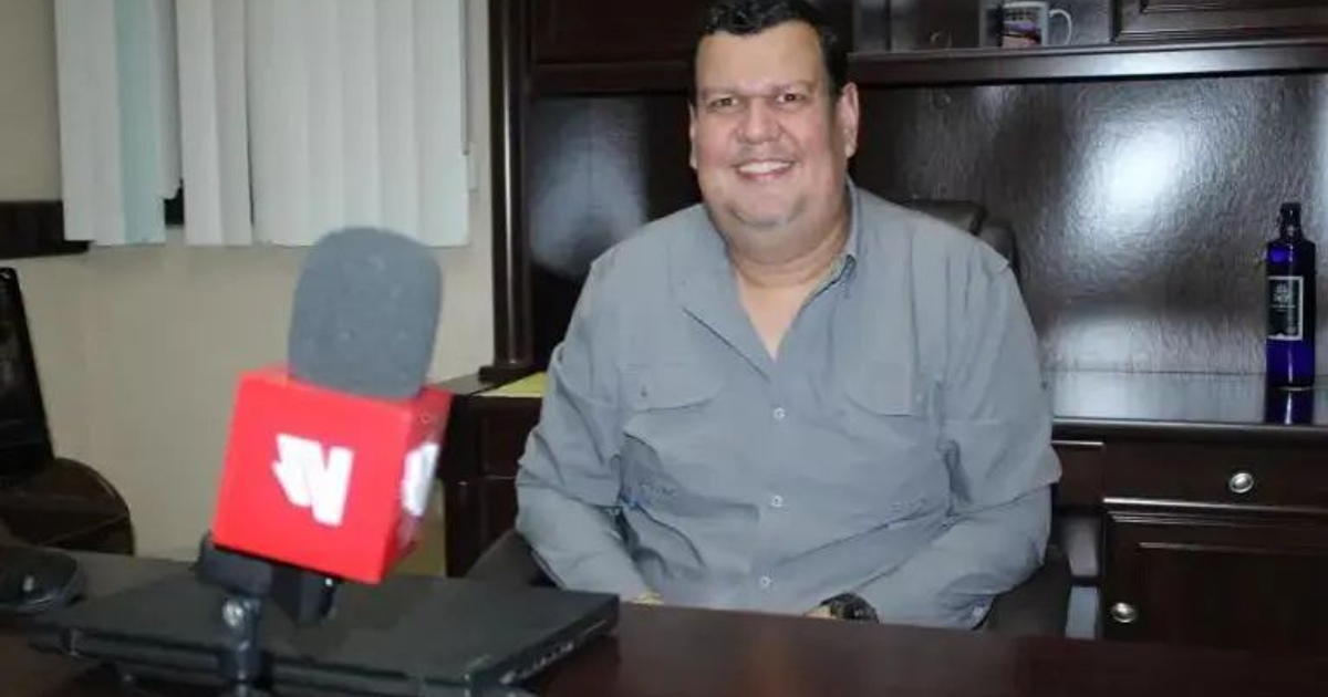 Mauricio López Quevedo en su oficina con micrófono y estanterías de fondo