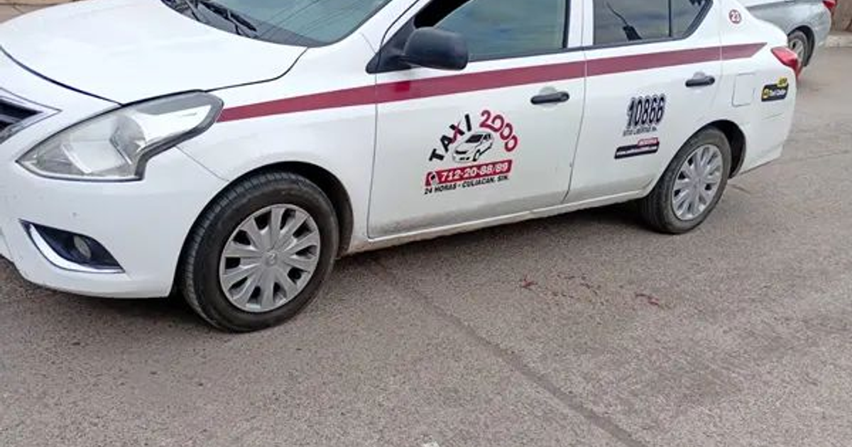 Taxi blanco con detalles rojos abandonado en Culiacán, Sinaloa, con llanta desinflada.