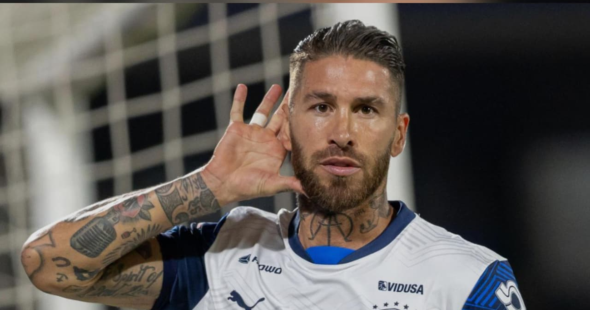 Sergio Ramos en el campo, gesticulando hacia el público, con tatuajes visibles y una red de portería al fondo.