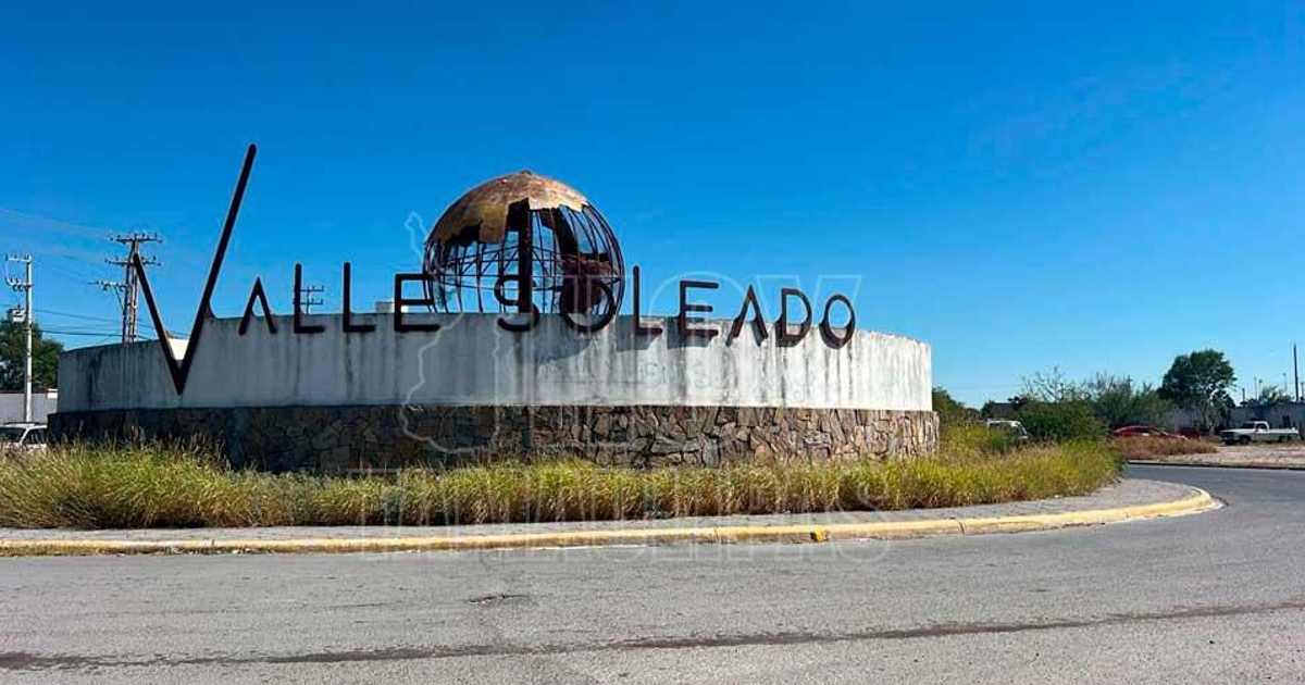 Glorieta en Valle Soleado con muro de piedra y globo terráqueo de metal, cielo azul y plantas verdes.