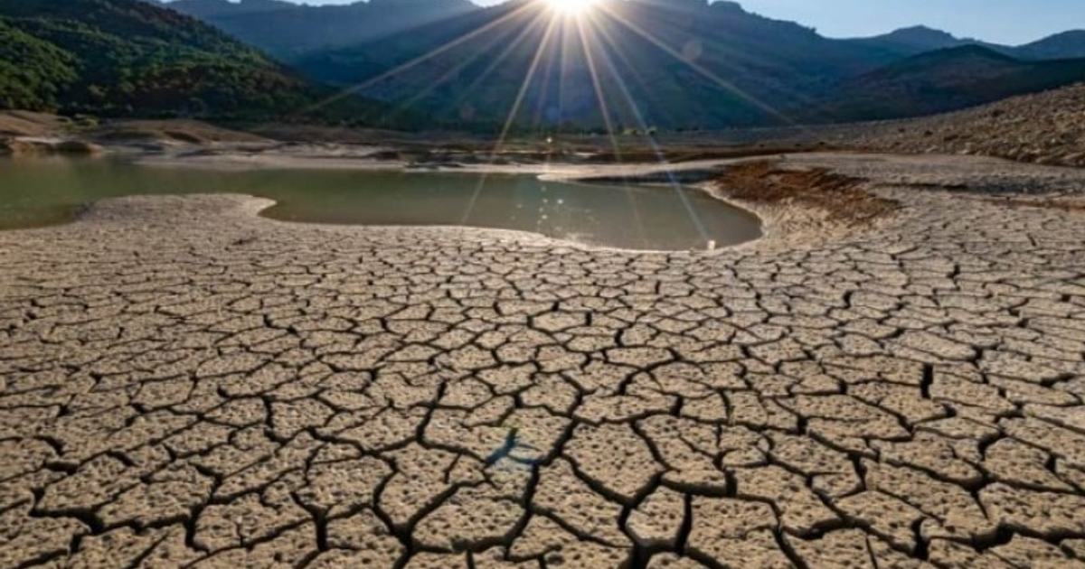 Paisaje seco y agrietado en Sinaloa con montañas y sol brillante, reflejando la sequía proyectada por el SMN.