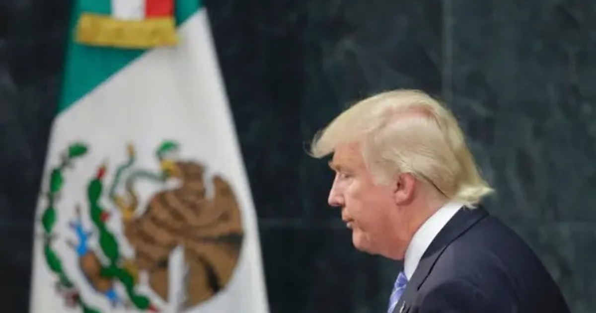 Persona de perfil frente a la bandera de México en un evento formal