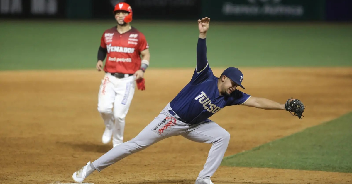 Jugador de béisbol en uniforme azul intenta atrapar la bola mientras otro en uniforme rojo corre en el campo.