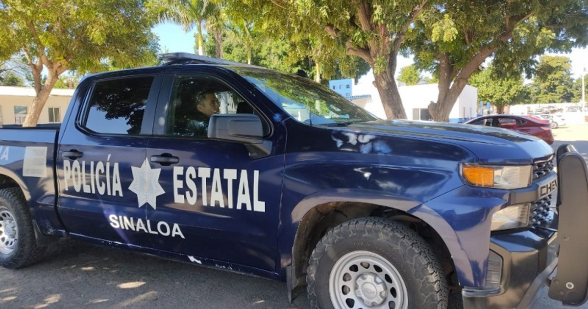 Camioneta de la Policía Estatal de Sinaloa estacionada, con una persona al volante, en un área con árboles y edificios al fondo.