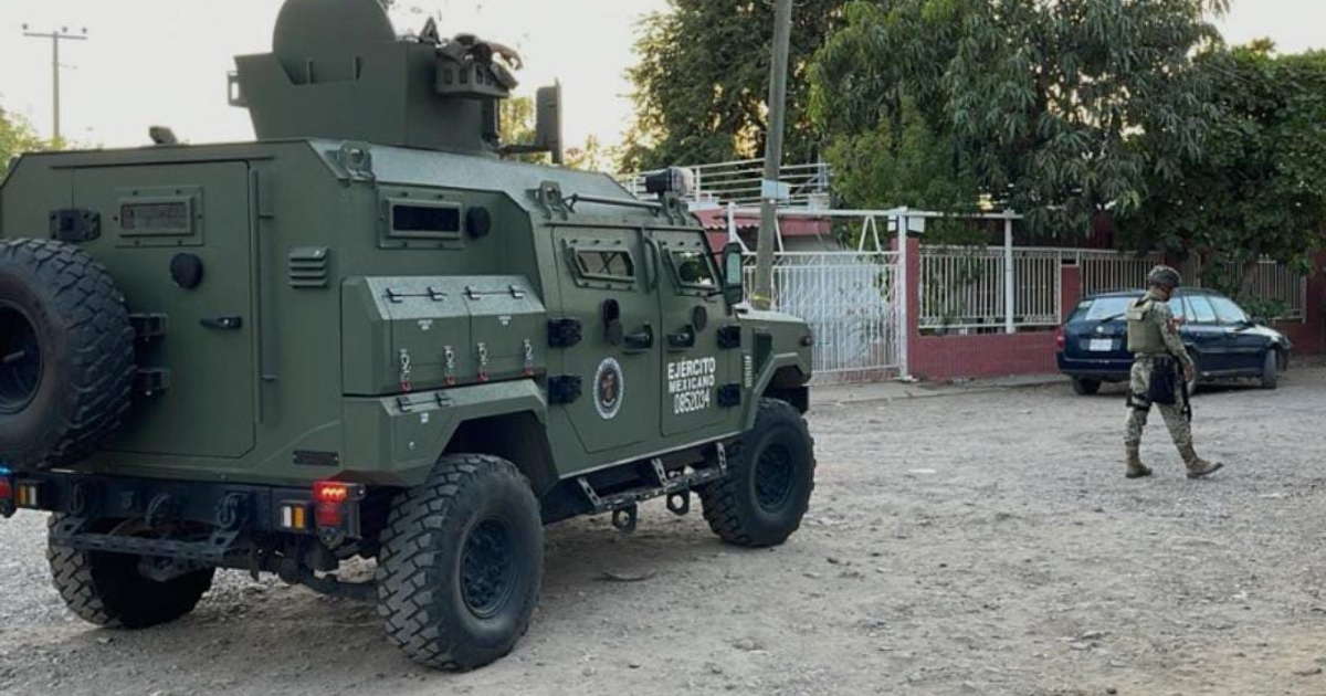 Vehículo militar verde con insignias y soldado en uniforme caminan junto a edificios urbanos en Culiacán.