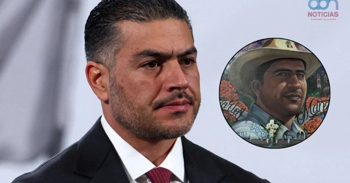 Hombre en traje junto a pintura de hombre con sombrero, fondo floral, homenaje a Carlos Manzo.