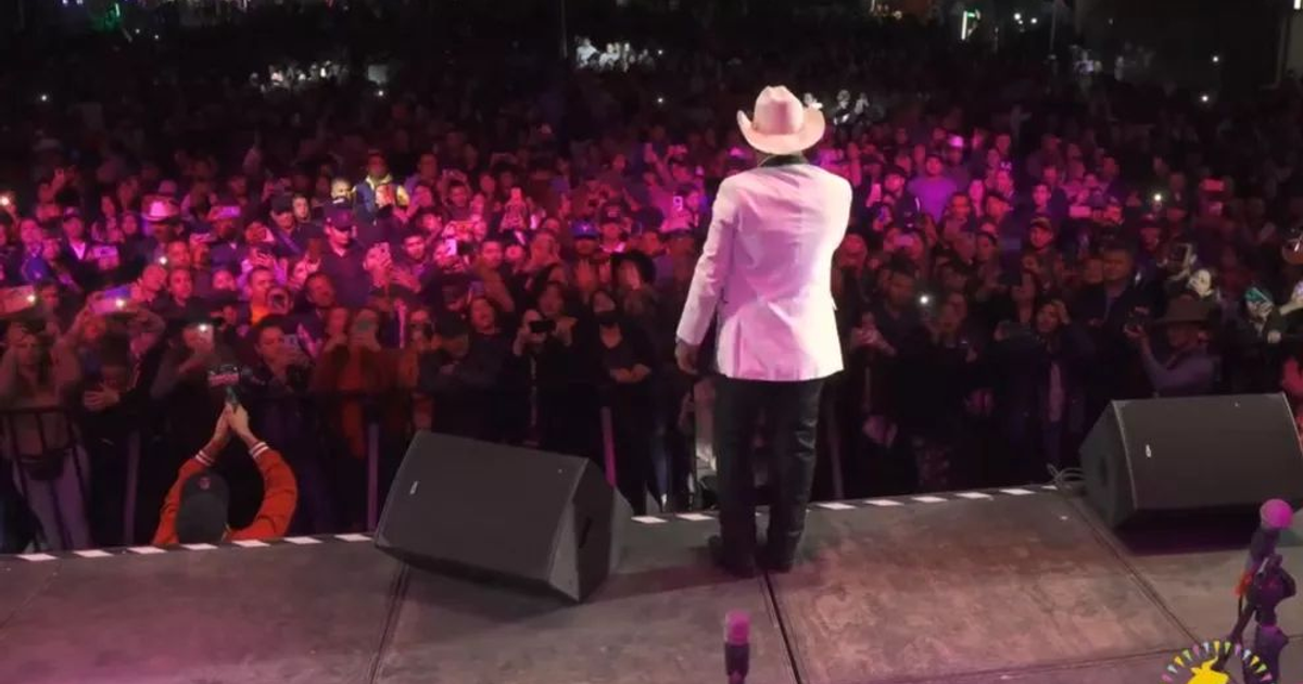 Artista en traje blanco actuando en la Feria Ganadera 2025 ante un público con luces de móviles.