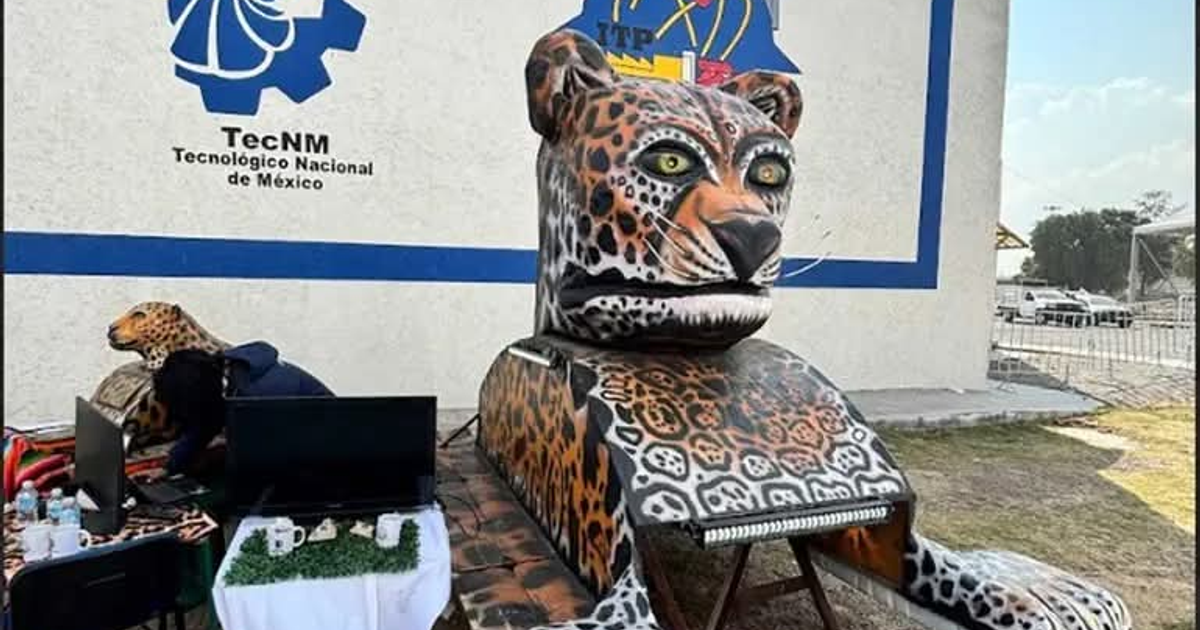 Escultura de jaguar en exhibición, fondo institucional con persona trabajando en computadora