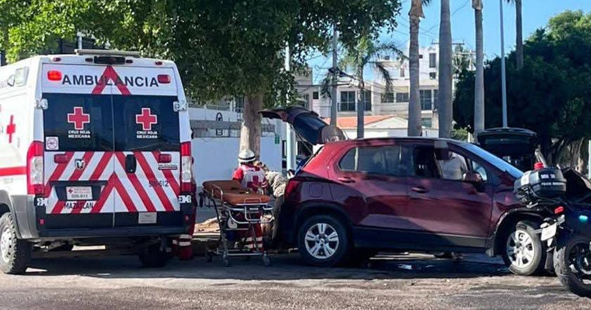 Ambulancia de la Cruz Roja Mexicana junto a coche rojo en accidente vehicular, con paramédico y moto de policía en Mazatlán.
