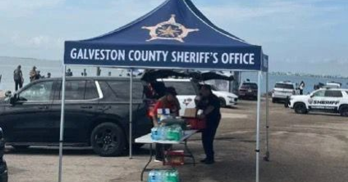 Toldo del Galveston County Sheriff con vehículos policiales y personas interactuando en un entorno playero.