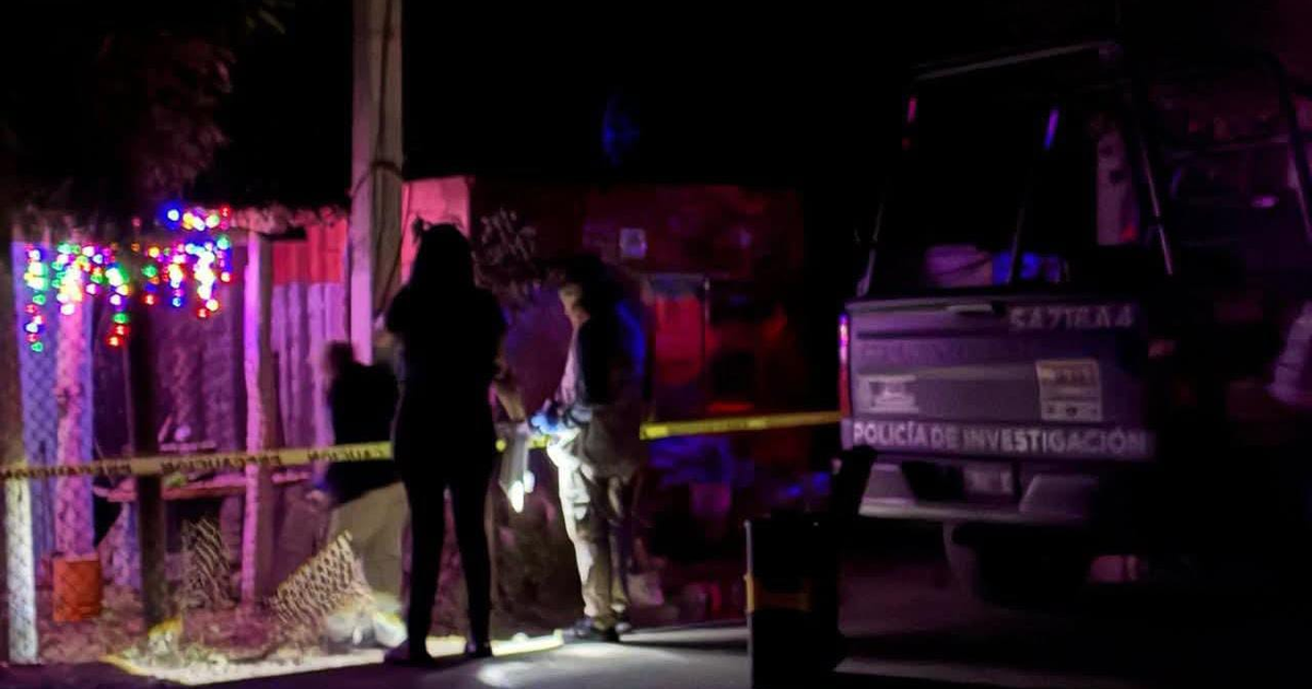Agente de investigación en escena nocturna de homicidio en Navolato, Sinaloa, con luces decorativas y vehículo de policía bajo cinta amarilla.