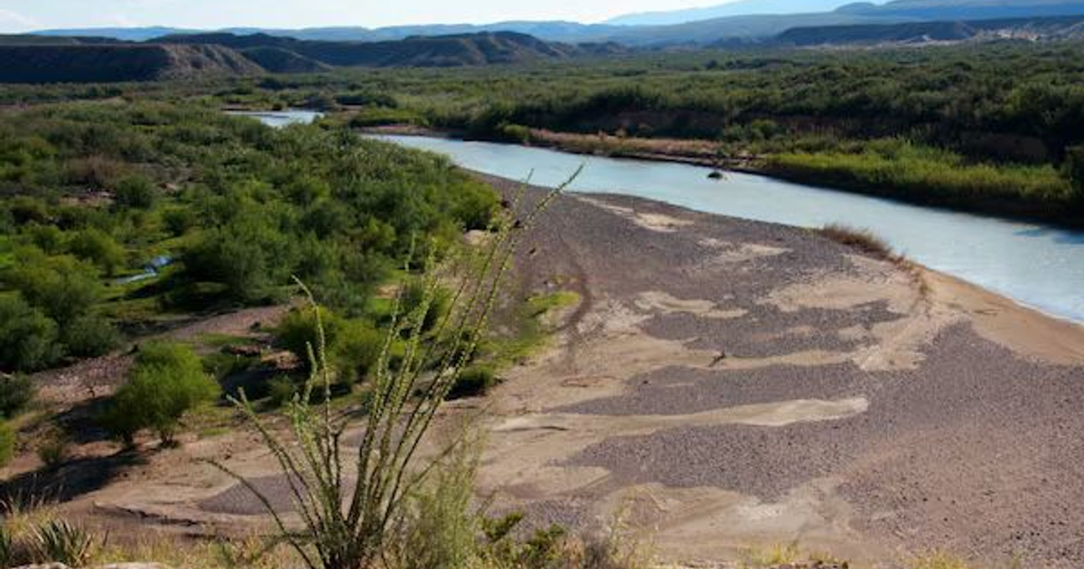 Río entre vegetación densa y colinas lejanas bajo un cielo despejado.