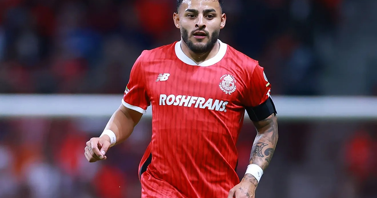 Jugador de fútbol del Toluca en acción, con camiseta roja y fondo de estadio.