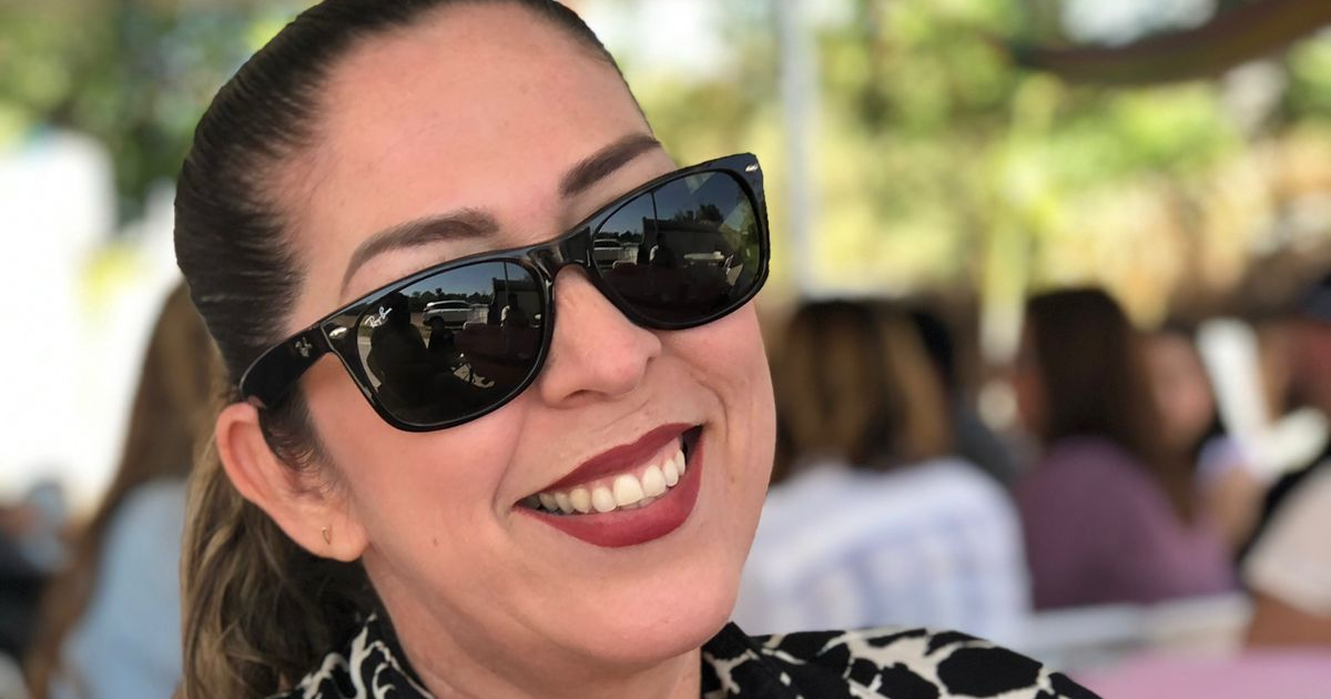 Mujer sonriente con gafas de sol en exterior, símbolo de esperanza y apoyo en su batalla de salud.