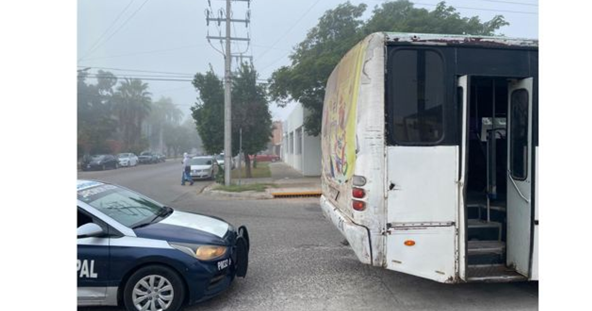Autobús urbano estacionado en un callejón con un coche de policía al frente, bajo clima nublado.