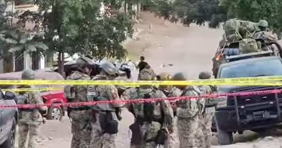 Soldados con uniformes de camouflage en Culiacán con vehículos de seguridad y árboles al fondo.