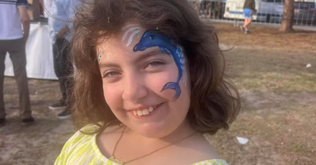 Niña sonriente con pintura de delfín en mejilla durante evento al aire libre