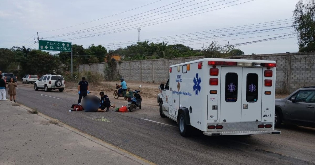 Ambulancia en una carretera con personas auxiliando a un herido cerca de un letrero hacia Tepic y El Recodo.