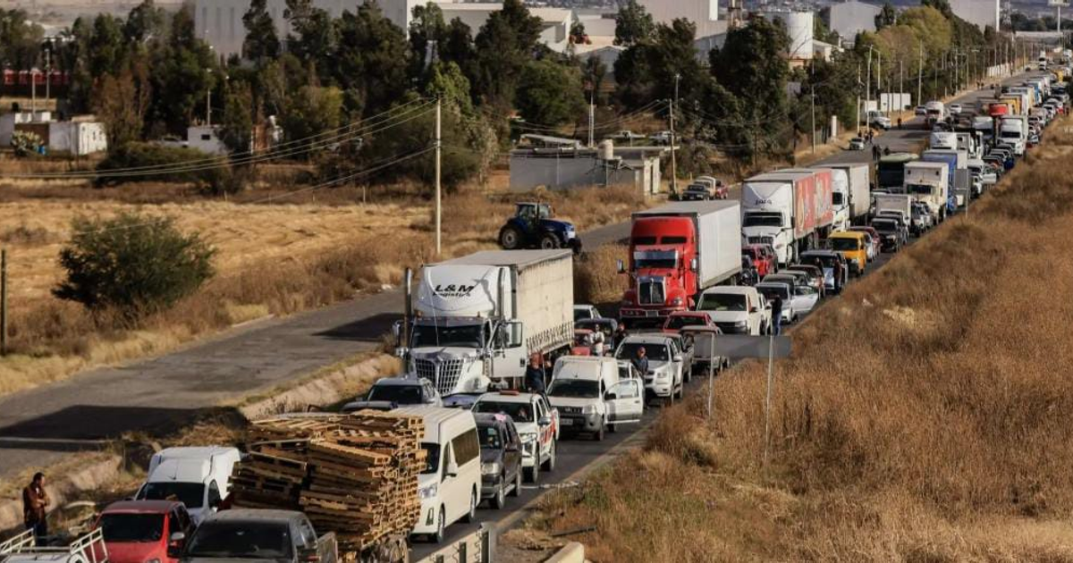 Tráfico intenso en carretera con vehículos alineados y áreas rurales de fondo