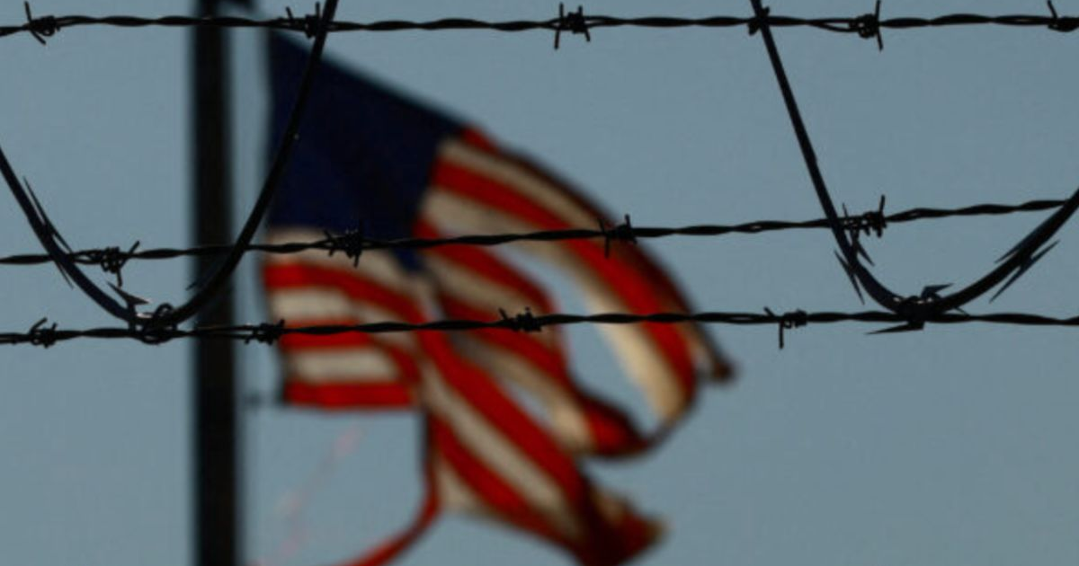 Bandera de Estados Unidos con alambre de púas en primer plano, simbolizando restricciones.