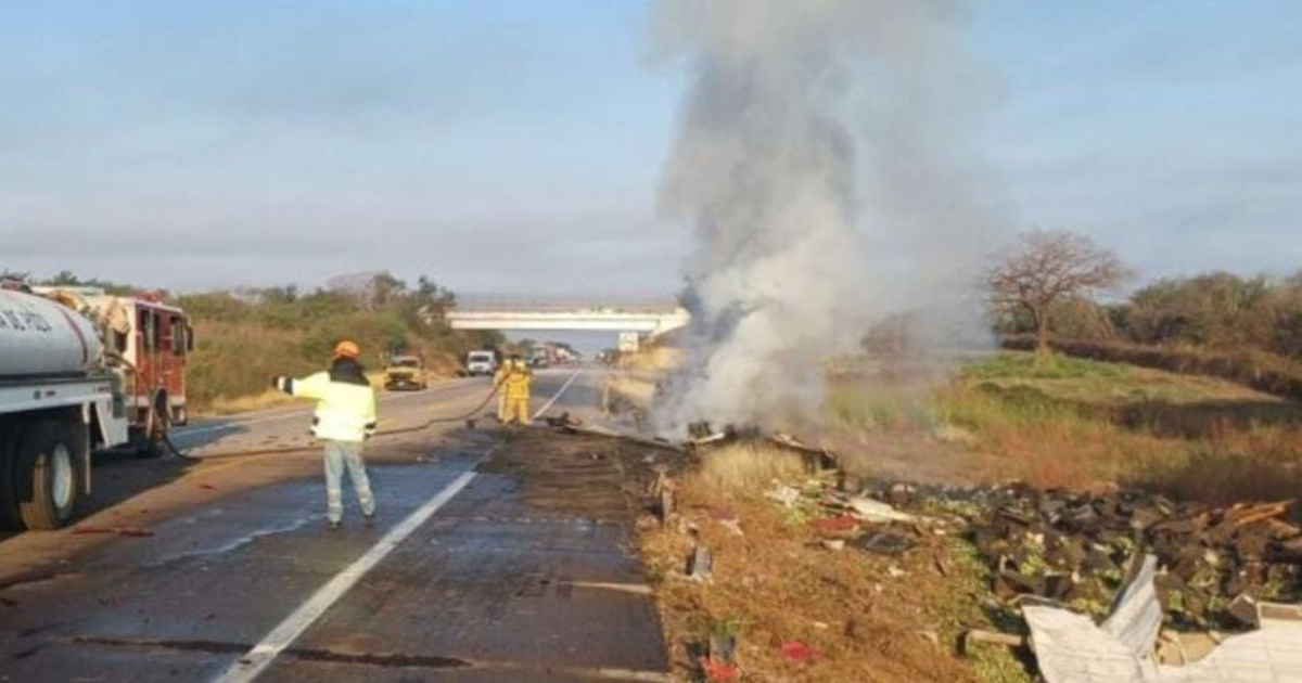 Escena de accidente con humo visible en autopista, camión de bomberos y personal de emergencia presentes.