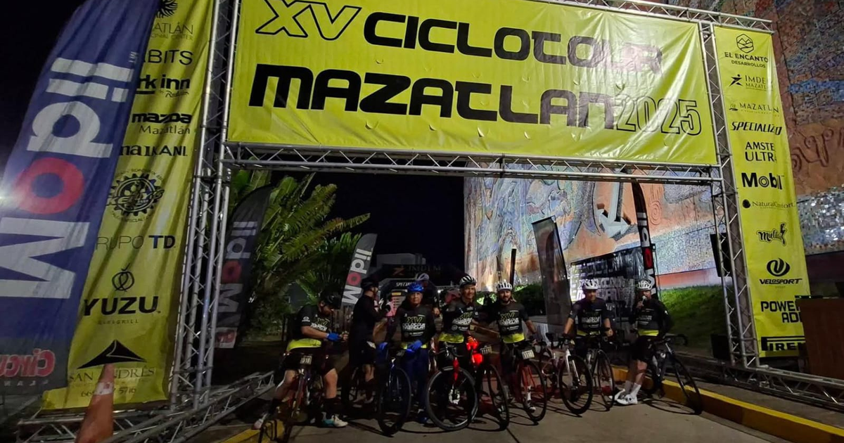 Ciclistas posando bajo el arco del Ciclotour Mazatlán 2025 en un evento nocturno.