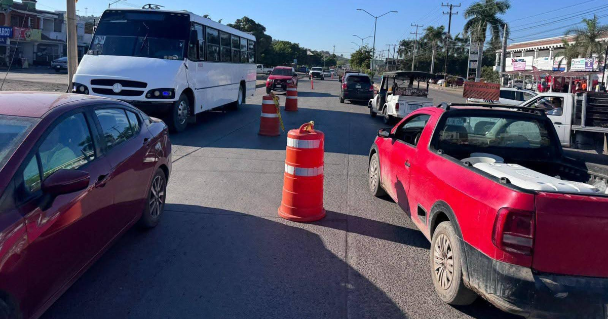 Congestión vehicular en ciudad con autobús blanco y barricas de obras