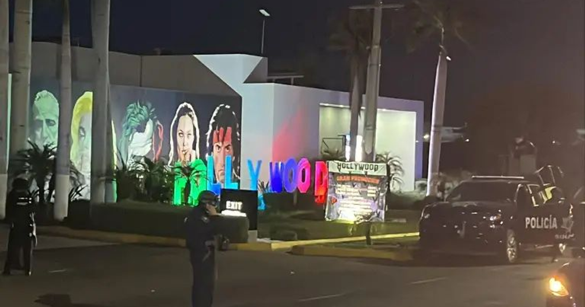 Letrero de Hollywood iluminado nocturnamente, con patrulla de policía y personaje de seguridad en primer plano.