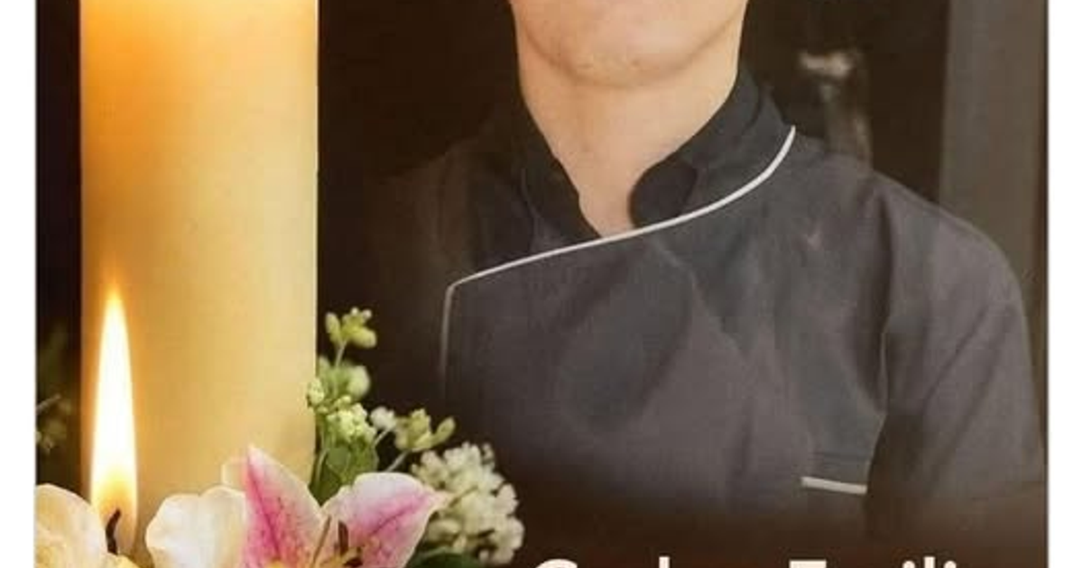 Persona en atuendo de chef con vela y flores en tributo solemne.