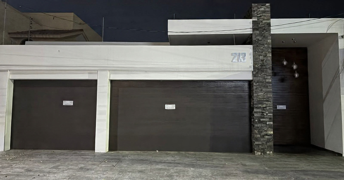 Fachada de edificio moderno con dos puertas de garage oscuras y entrada principal de piedra. Operativo nocturno en colonia Guadalupe, Culiacán.
