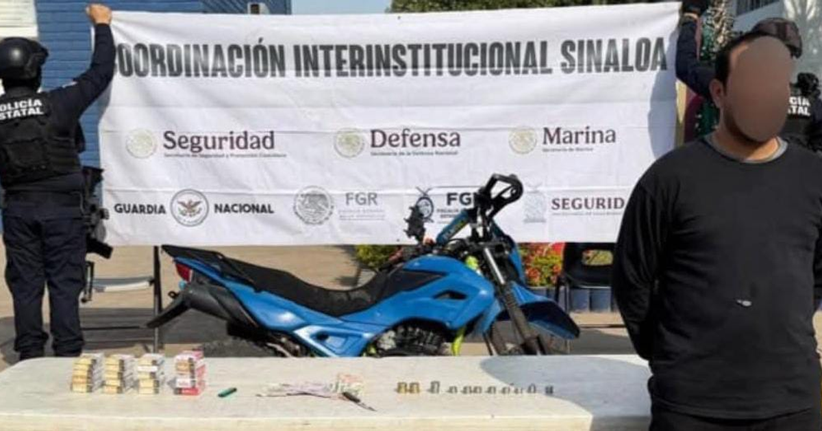 Hombre detenido frente a una mesa con evidencias: dinero y motocicleta azul, en operativo de seguridad en Sinaloa.