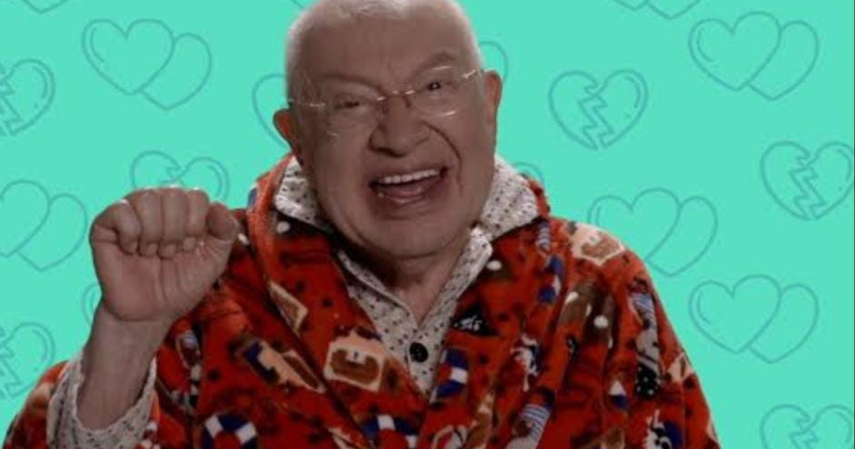 Eduardo Manzano sonriendo, con bata roja y fondo azul con corazones