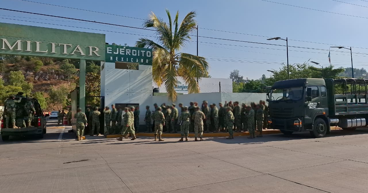Soldados del Ejército Mexicano alineados por un portón en la Tercera Región Militar en Mazatlán con un vehículo militar cercano, árboles y clima soleado.