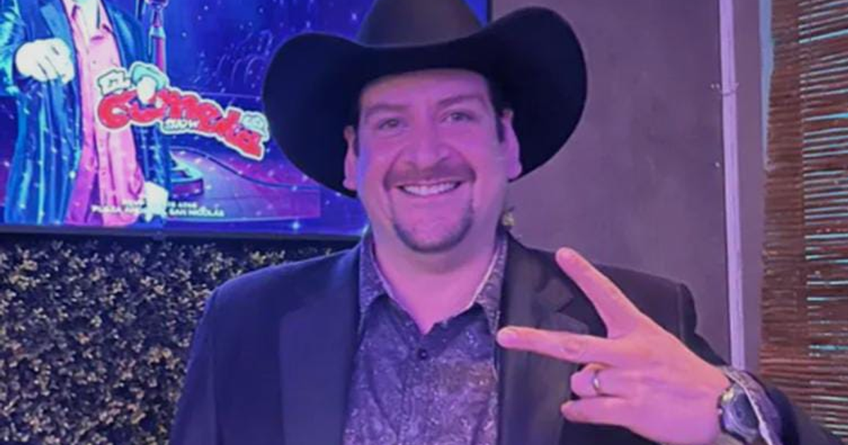 Jesús González, 'El Cometa Show', sonriendo con un sombrero negro y traje oscuro, gesto de paz y fondo de show de comedia colorido.