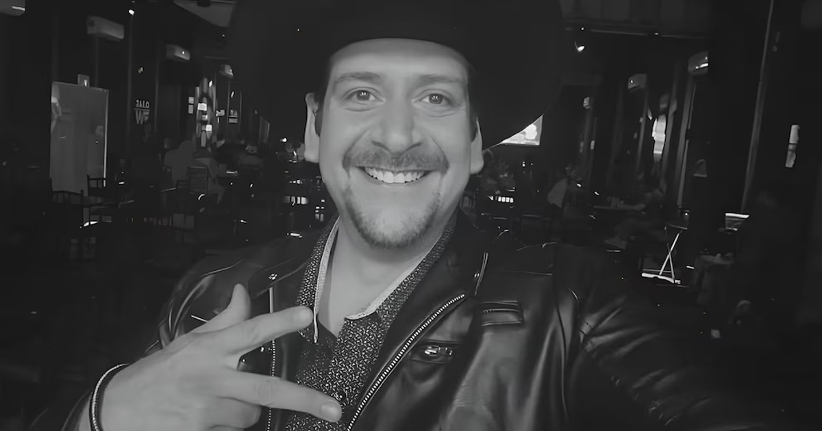 Jesús Alberto González 'El Cometa Show' sonriendo en un restaurante, vestido de chaqueta negra y sombrero, capturado en una nostálgica imagen en blanco y negro.