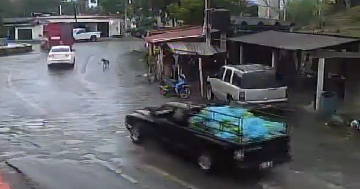 Escena de una calle urbana en Coahuayana con vehículos y estructuras, destacando una camioneta negra vinculada a un traslado de explosivos.