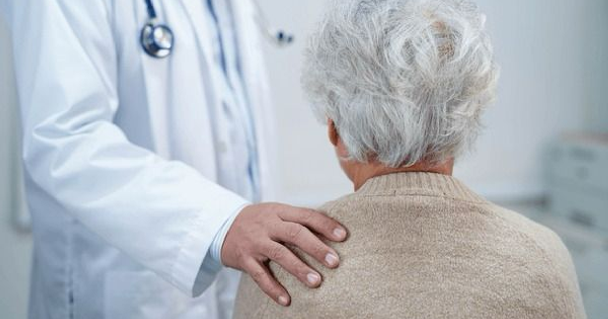 Profesional de la salud tocando el hombro de una persona mayor en un consultorio médico