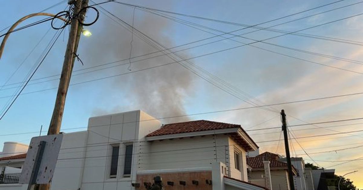 Paisaje urbano al atardecer con una casa con techo de tejas y humo saliendo de una chimenea, aludiendo al incendio en Chapultepec, Culiacán.