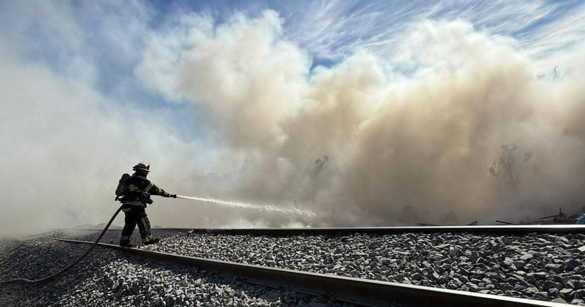 Un bombero maneja una manguera en un incendio en las vías del tren