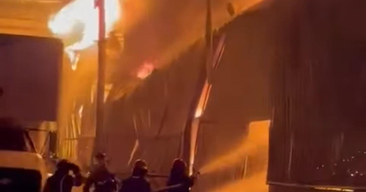 Bomberos combatiendo incendio en fábrica de colchones en Ixtapaluca, llamas intensas iluminan la noche.