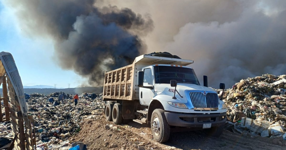 Camión de basura en vertedero de Culiacán durante incendio, con columna de humo negro al fondo.