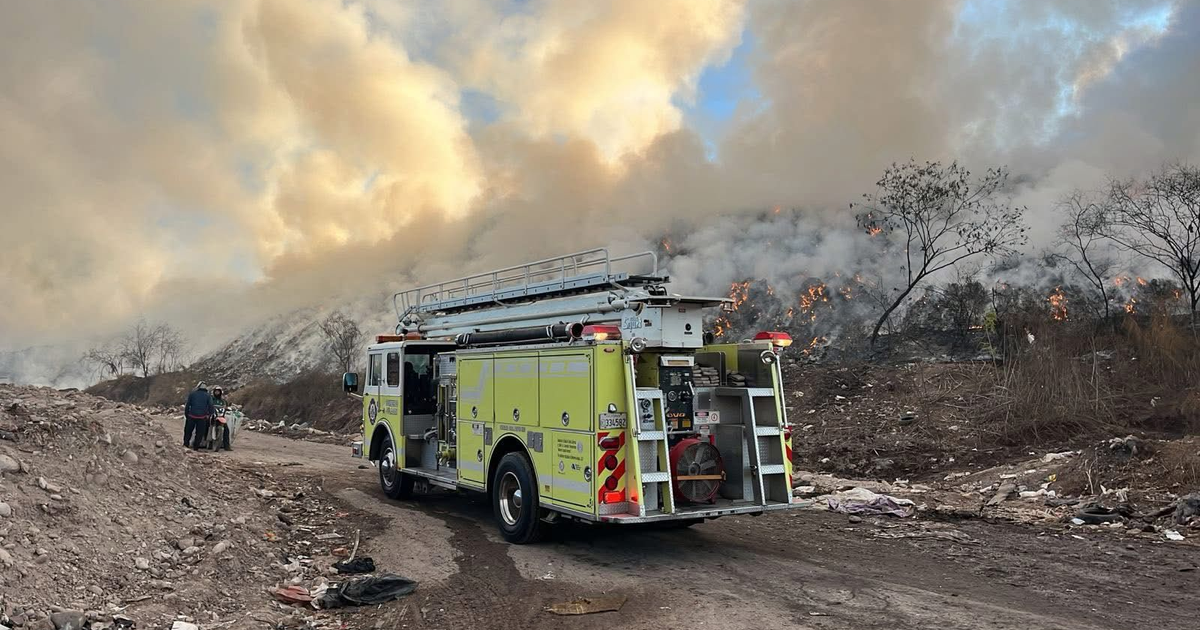 Camión de bomberos amarillo con un incendio al fondo, trabajando en el basurón de Culiacán.