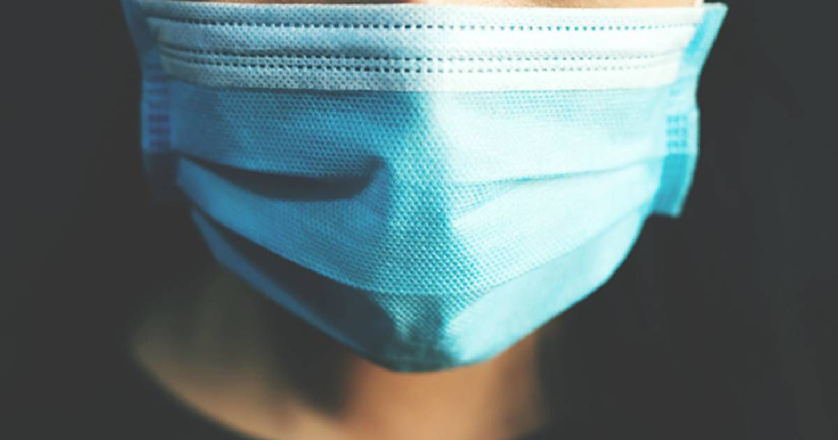 Rostro con mascarilla azul en primer plano sobre fondo oscuro.