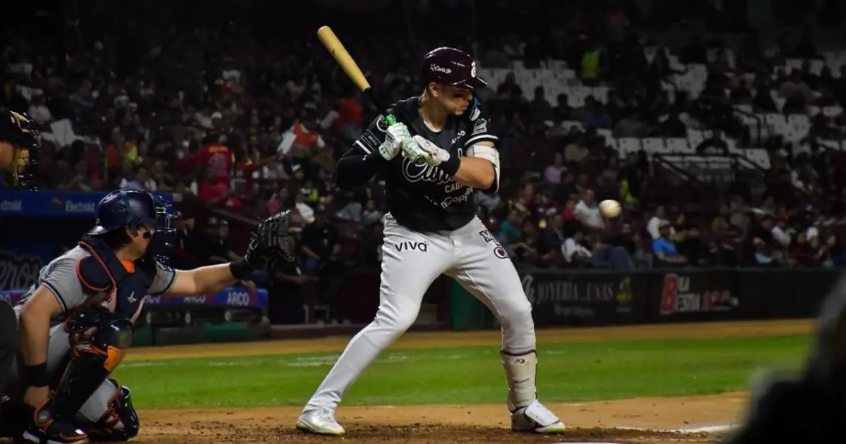 Jugador de béisbol de los Jaguares de Nayarit preparándose para batear, receptor al fondo, estadio lleno.
