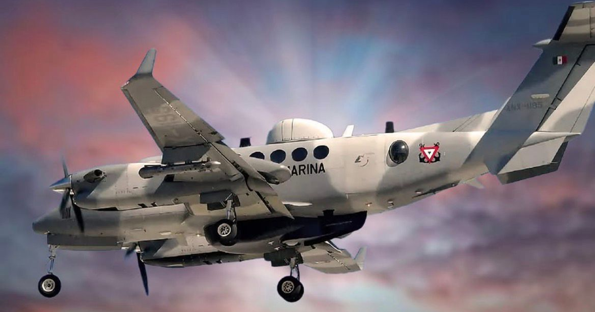 Avión militar gris de la Armada de México volando al atardecer con nubes visibles.