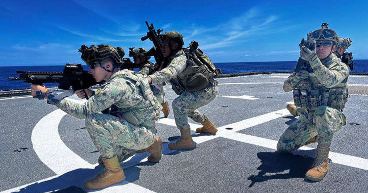 Soldados armados en posición táctica sobre la cubierta de un buque, con el mar y cielo azul al fondo.
